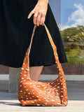 Person holding a brown bambi patterned cowhide handbag with white pattern outdoors