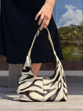 Person holding a zebra-patterned cowhide handbag outdoors