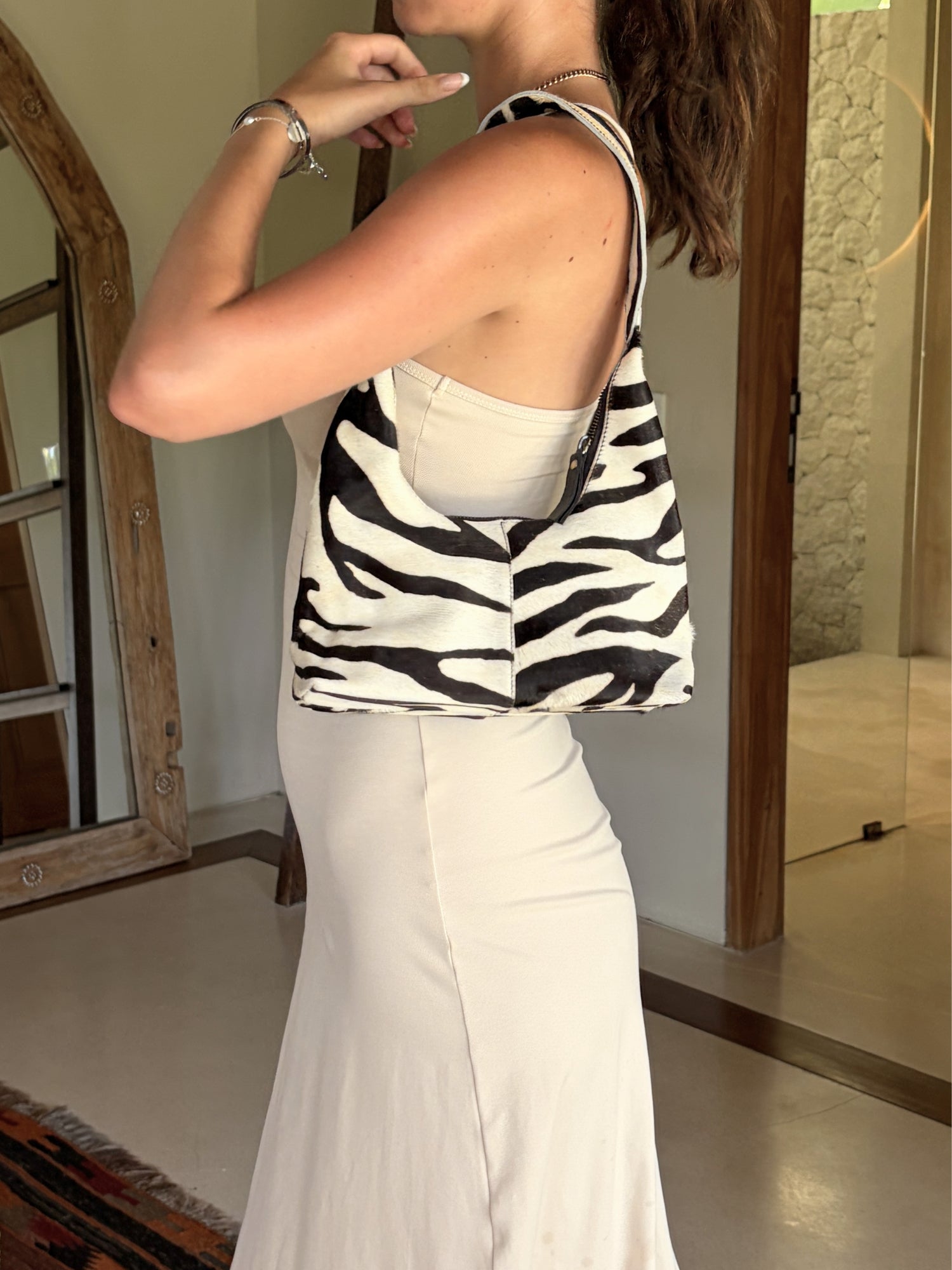 Person holding a zebra-striped cowhide handbag in a room with a mirror and textured wall.