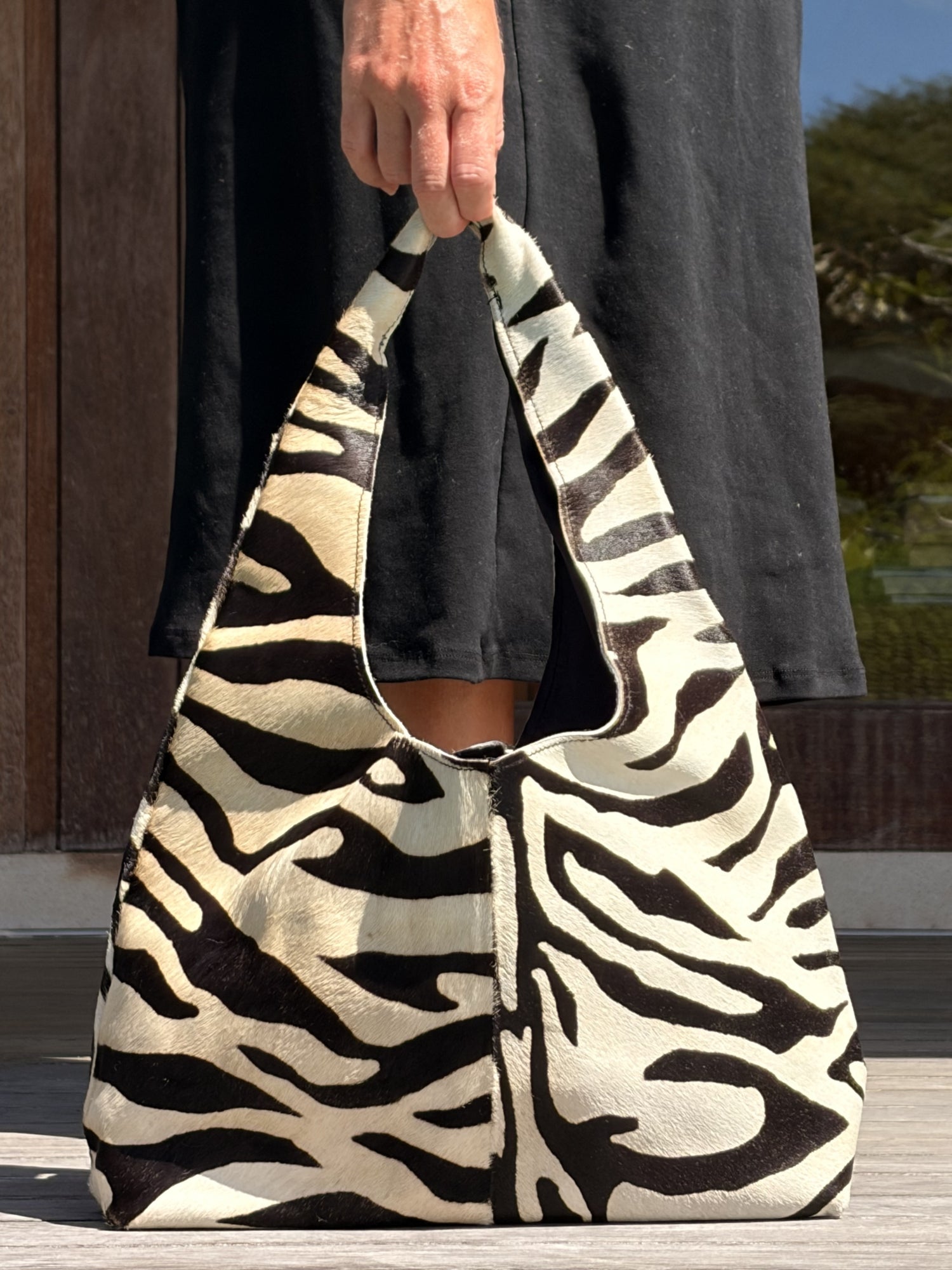 Hand holding a zebra-patterned cowhide shoulder bag outdoors