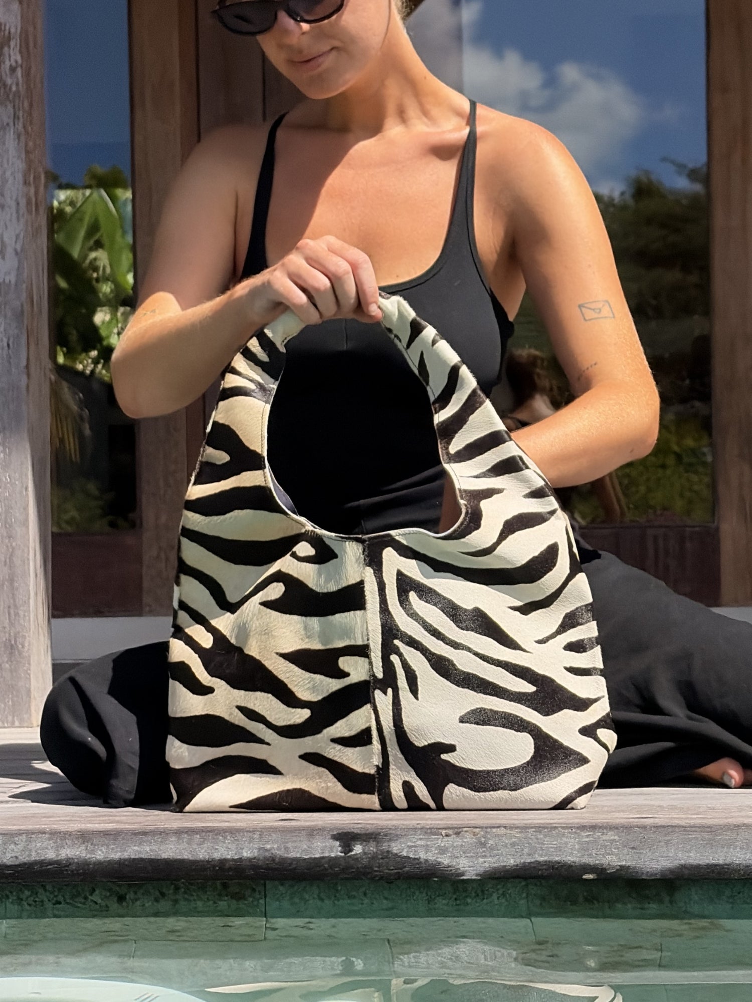 Woman holding a zebra-striped cowhide bag by a pool